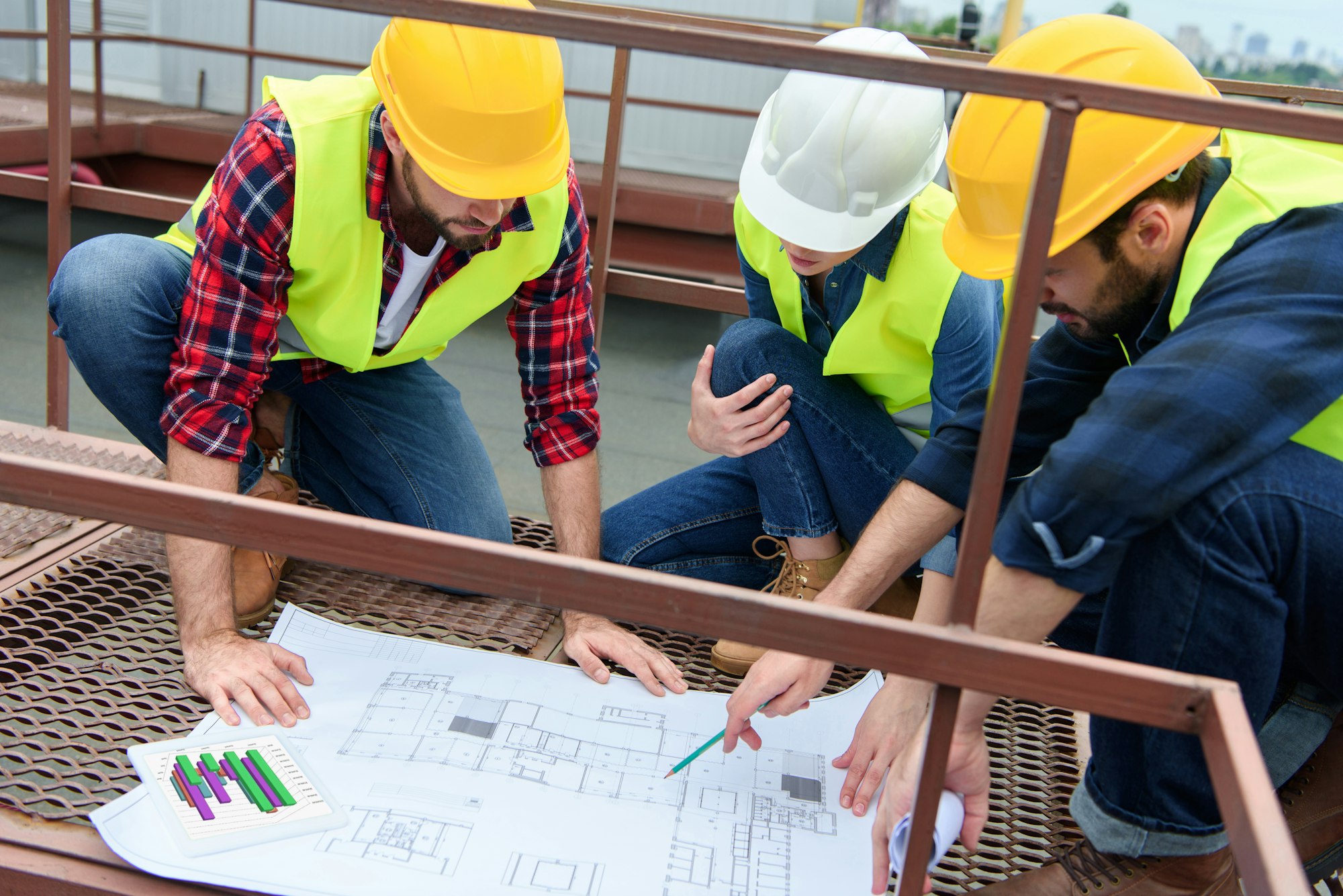 three architects in hardhats working with blueprints on roof